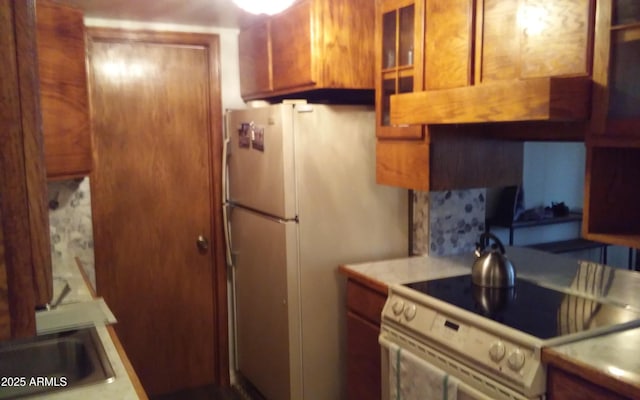 kitchen with brown cabinetry, electric stove, glass insert cabinets, freestanding refrigerator, and light countertops