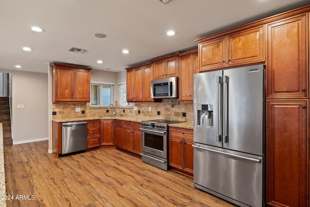 kitchen featuring sink, light stone countertops, appliances with stainless steel finishes, light hardwood / wood-style floors, and tasteful backsplash