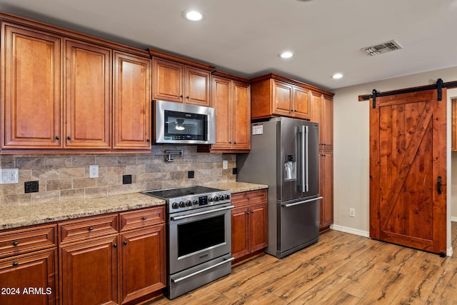 kitchen with backsplash, a barn door, light stone countertops, premium appliances, and light hardwood / wood-style floors