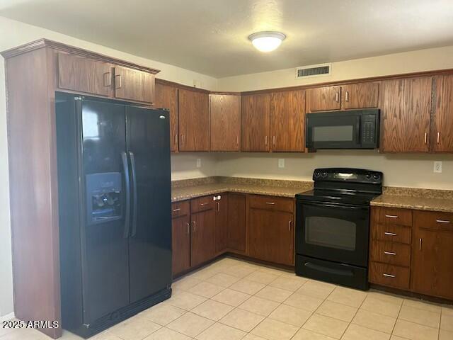 kitchen with dark stone countertops, light tile patterned floors, dark brown cabinetry, and black appliances