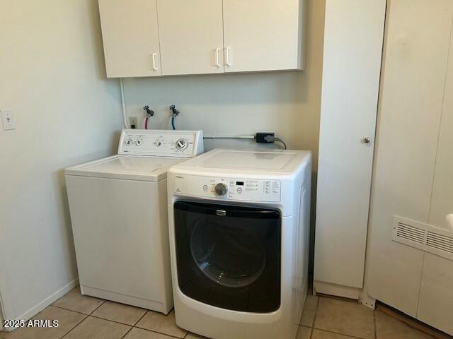 clothes washing area featuring cabinets, light tile patterned floors, and washer and clothes dryer