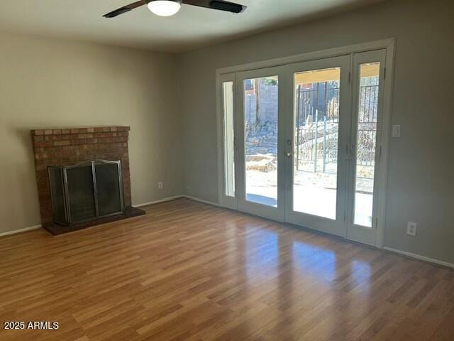 unfurnished living room with a brick fireplace, wood-type flooring, and ceiling fan