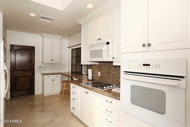 kitchen featuring tasteful backsplash, dark stone countertops, white cabinets, light tile patterned floors, and white appliances