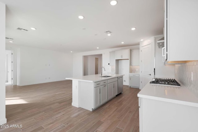 kitchen with sink, appliances with stainless steel finishes, light hardwood / wood-style floors, an island with sink, and decorative backsplash