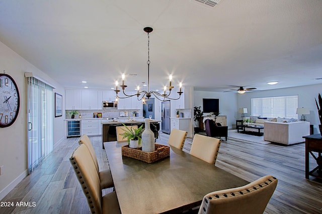 dining area featuring beverage cooler, light hardwood / wood-style floors, and ceiling fan with notable chandelier