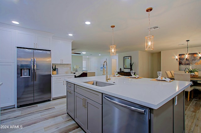 kitchen with sink, hanging light fixtures, stainless steel appliances, an island with sink, and white cabinets