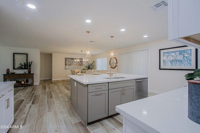 kitchen featuring light wood-type flooring, stainless steel dishwasher, gray cabinetry, decorative light fixtures, and a center island with sink