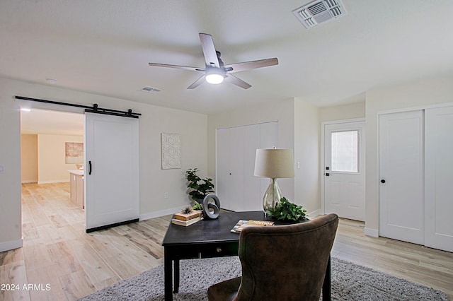 office space featuring a barn door, ceiling fan, and light wood-type flooring