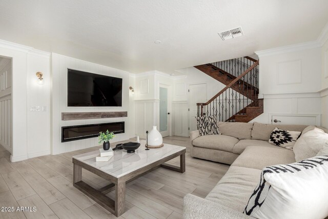 living room with visible vents, light wood-type flooring, stairs, and a decorative wall