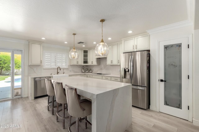 kitchen with appliances with stainless steel finishes, a center island, light wood finished floors, a sink, and visible vents