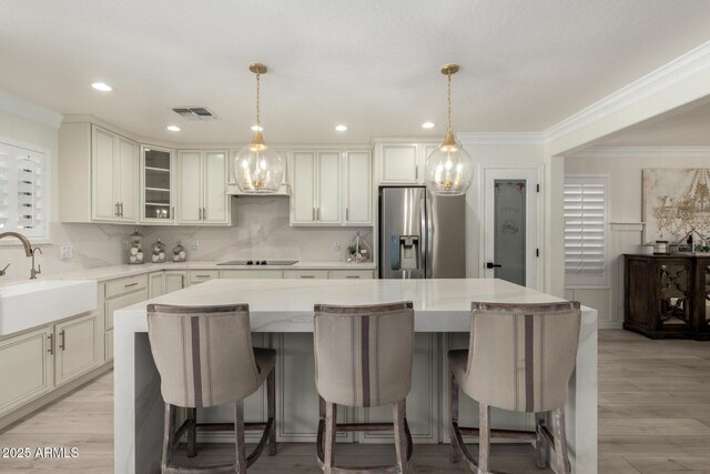 kitchen featuring a sink, a center island, ornamental molding, black electric cooktop, and stainless steel refrigerator with ice dispenser