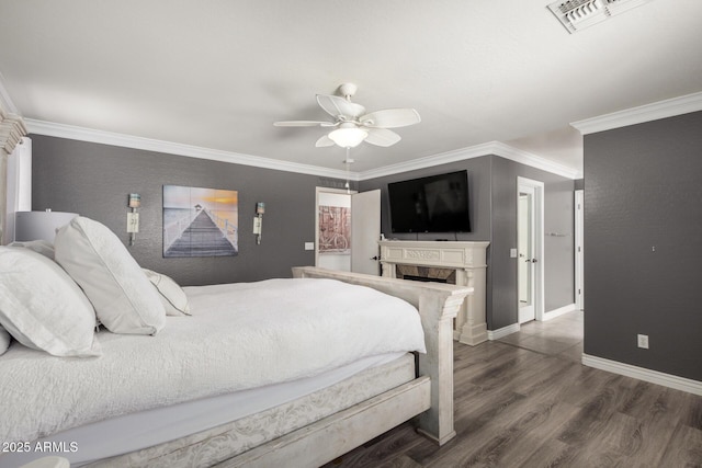 bedroom with a fireplace, crown molding, visible vents, baseboards, and wood finished floors