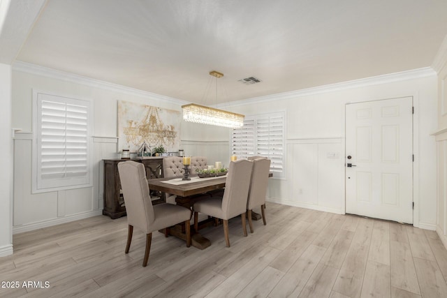 dining area featuring light wood finished floors, a wainscoted wall, visible vents, and a decorative wall