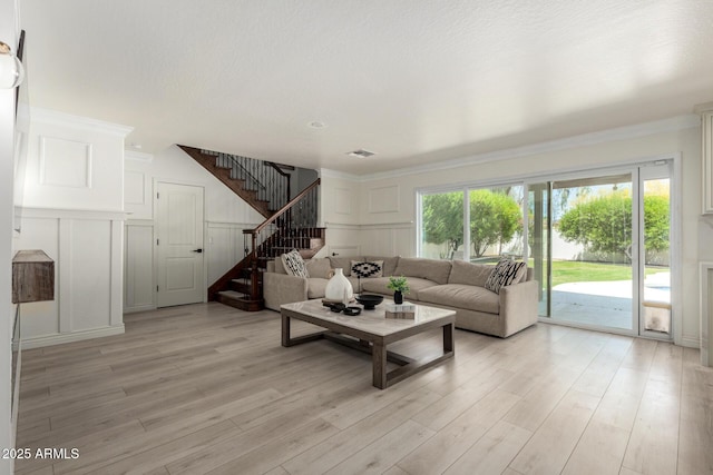living room featuring light wood-type flooring, stairs, and a decorative wall