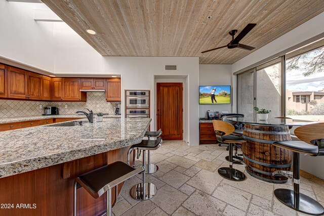 kitchen featuring backsplash, wooden ceiling, sink, ceiling fan, and a breakfast bar