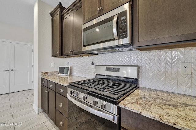 kitchen with light stone countertops, dark brown cabinets, tasteful backsplash, and appliances with stainless steel finishes
