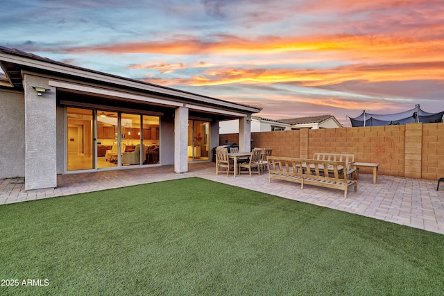 back of house at dusk with a patio area, stucco siding, fence, and a lawn