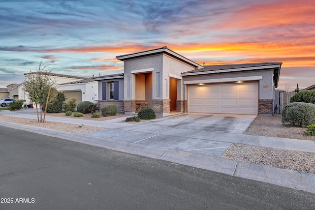 view of front of property featuring a tile roof, stucco siding, driveway, brick siding, and a garage