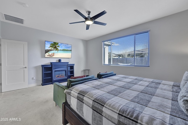 bedroom with a glass covered fireplace, visible vents, carpet flooring, and a ceiling fan