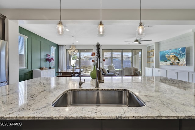 kitchen with built in shelves, a sink, light stone counters, pendant lighting, and freestanding refrigerator