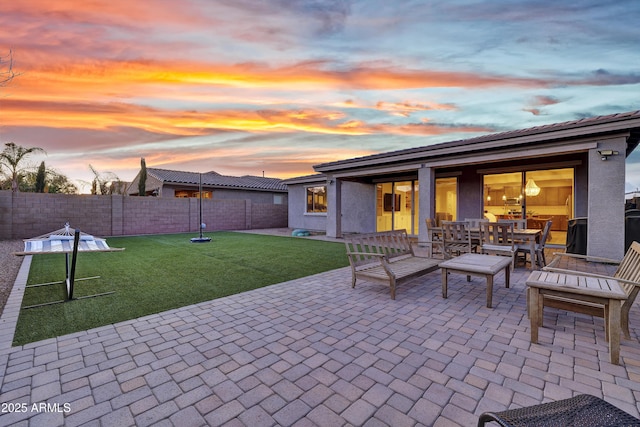 patio terrace at dusk featuring a fenced backyard and a yard