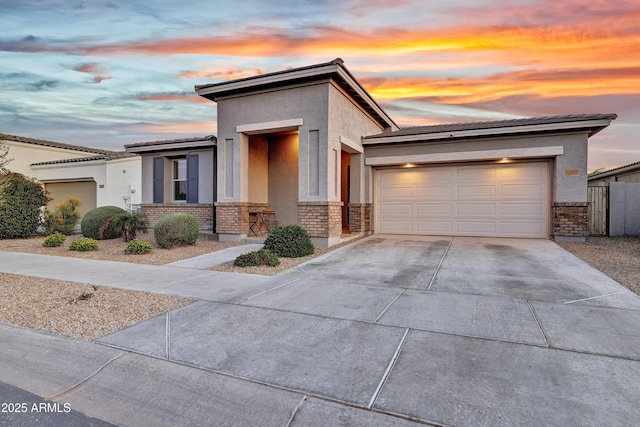 view of front of house featuring driveway, a tiled roof, a garage, brick siding, and stucco siding