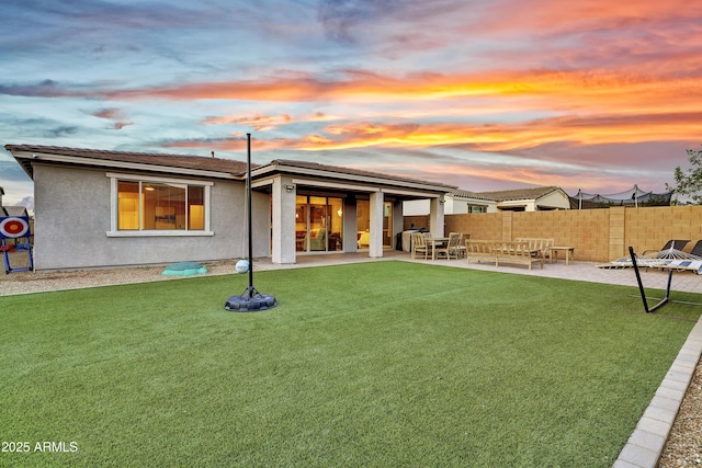 back of house at dusk featuring a yard, stucco siding, fence, and a patio