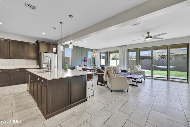 kitchen with decorative backsplash, a sink, dark brown cabinetry, and visible vents
