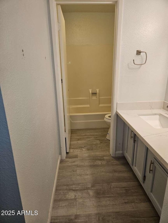 bathroom featuring toilet, a bathing tub, wood finished floors, vanity, and baseboards