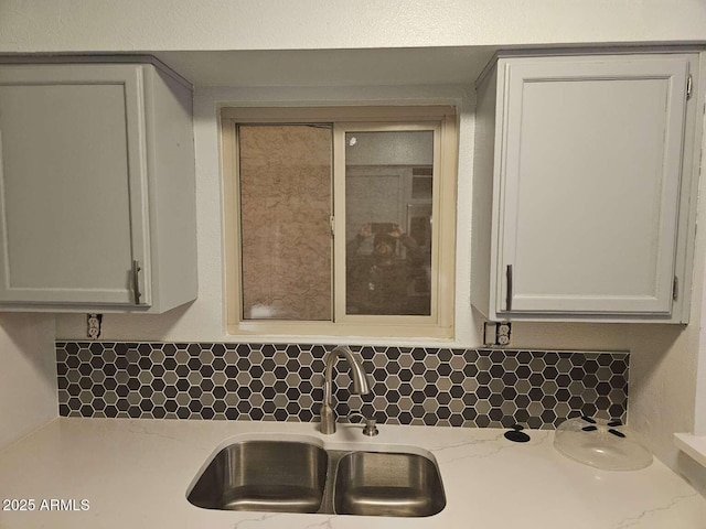 kitchen featuring a sink, white cabinetry, backsplash, light stone countertops, and glass insert cabinets