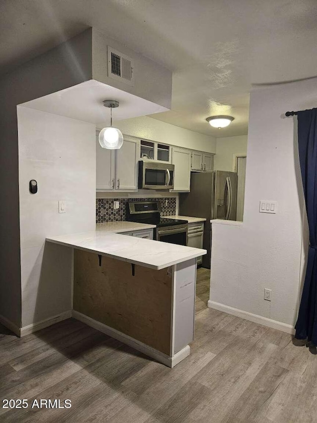 kitchen with visible vents, appliances with stainless steel finishes, a breakfast bar area, a peninsula, and light countertops