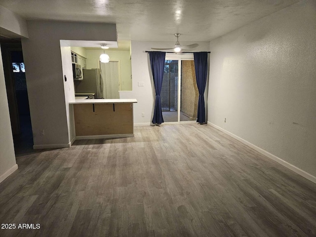 unfurnished living room featuring ceiling fan, baseboards, and wood finished floors