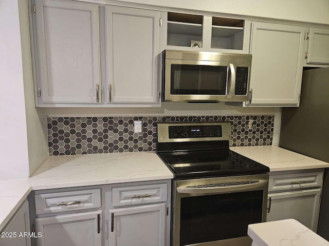 kitchen featuring stainless steel appliances, backsplash, and light stone counters