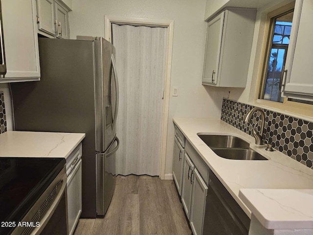 kitchen featuring light stone counters, tasteful backsplash, gray cabinets, a sink, and wood finished floors