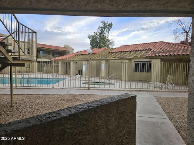 exterior space featuring a patio area, a tile roof, a community pool, and fence