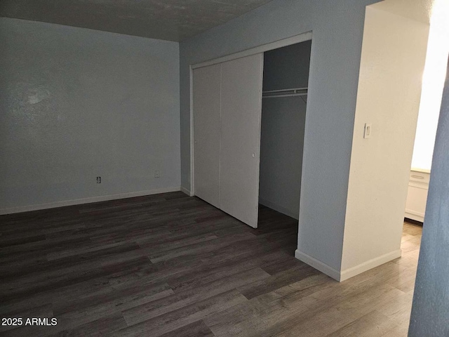 unfurnished bedroom with a closet, wood finished floors, and baseboards