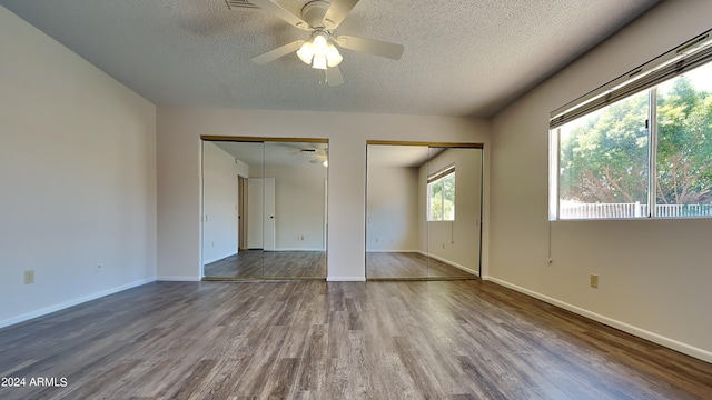 unfurnished bedroom with ceiling fan, hardwood / wood-style floors, a textured ceiling, and two closets