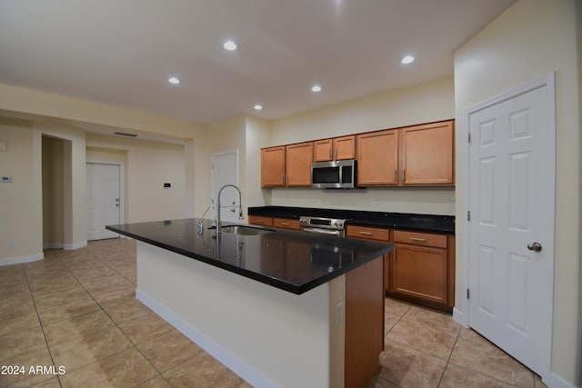 kitchen with appliances with stainless steel finishes, a kitchen island with sink, sink, and light tile floors