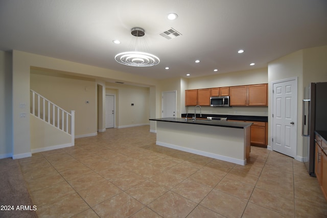 kitchen with decorative light fixtures, appliances with stainless steel finishes, light tile floors, and an island with sink