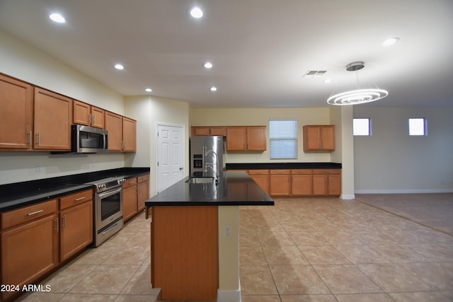 kitchen featuring a kitchen island with sink, sink, light tile floors, appliances with stainless steel finishes, and decorative light fixtures