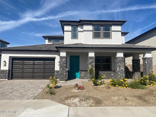 prairie-style house featuring stone siding, stucco siding, an attached garage, and decorative driveway