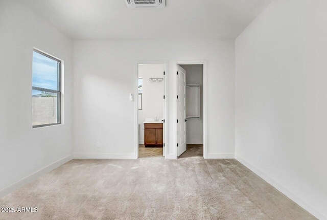 unfurnished bedroom with a spacious closet, visible vents, connected bathroom, baseboards, and carpet flooring