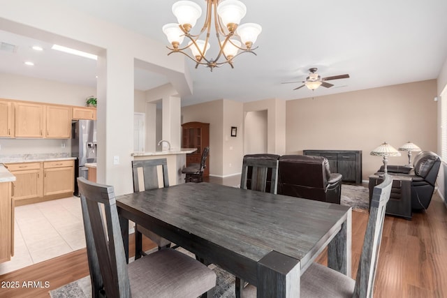 dining space with ceiling fan with notable chandelier and light hardwood / wood-style flooring