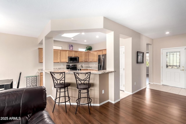 kitchen with a breakfast bar area, electric range, stainless steel fridge, kitchen peninsula, and light hardwood / wood-style floors