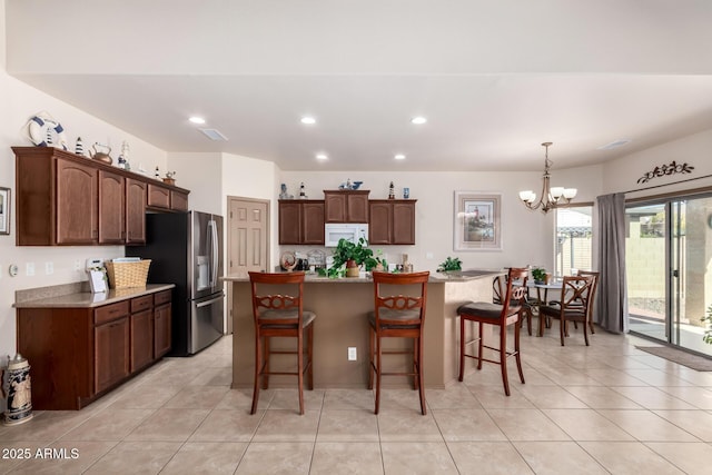 kitchen featuring an island with sink, a chandelier, a kitchen bar, stainless steel refrigerator with ice dispenser, and dark brown cabinets