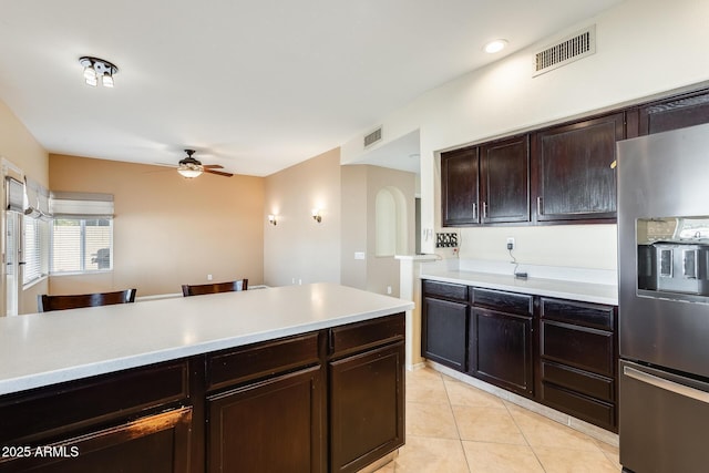 kitchen featuring light tile patterned floors, a breakfast bar area, ceiling fan, dark brown cabinets, and stainless steel fridge with ice dispenser