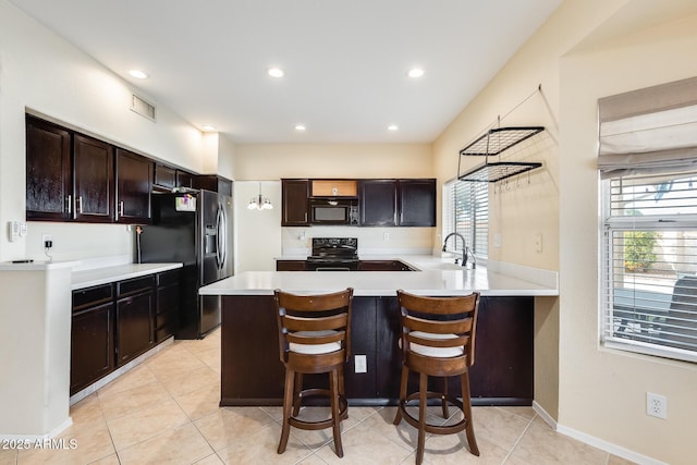 kitchen with a kitchen bar, sink, plenty of natural light, kitchen peninsula, and black appliances