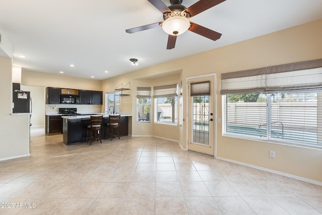 kitchen featuring light tile patterned flooring, a breakfast bar, a center island, electric range, and ceiling fan