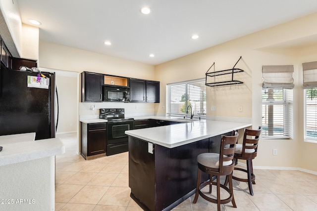 kitchen featuring sink, light tile patterned floors, black appliances, a kitchen bar, and kitchen peninsula