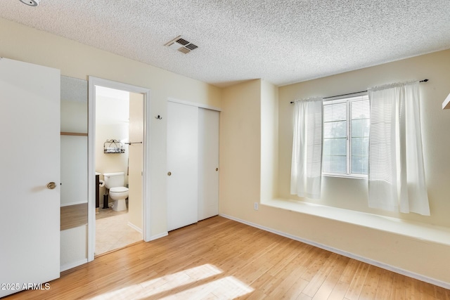 unfurnished bedroom with ensuite bathroom, hardwood / wood-style floors, a textured ceiling, and a closet